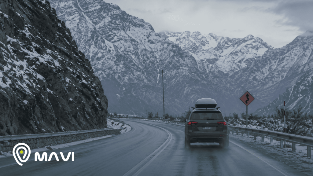 Vehículo circulando por una carretera de montaña rodeada de nieve durante el invierno. La imagen representa un viaje por carretera y la importancia de la seguridad en vacaciones de invierno.